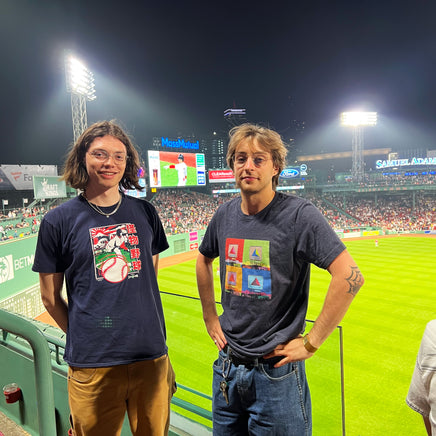 Photo inside fenway park of 2 men. one is wearing Navy blue unisex t-shirt with boston citgo sign design in colorful 4 up grid in the style of andy warhol