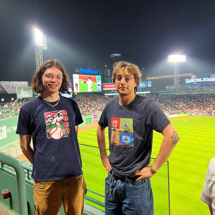 Photo inside fenway park of 2 men. one is wearing Navy blue unisex t-shirt with boston citgo sign design in colorful 4 up grid in the style of andy warhol