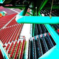 photo of fenway parks left field grandstand and field boxes in red and blue with the green metal structure of the building