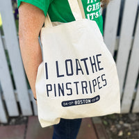 woman carrying tan canvas tote bag with the red sox phrase i loathe pinstripes by the red seat