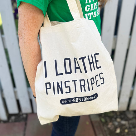 woman carrying tan canvas tote bag with the red sox phrase i loathe pinstripes by the red seat