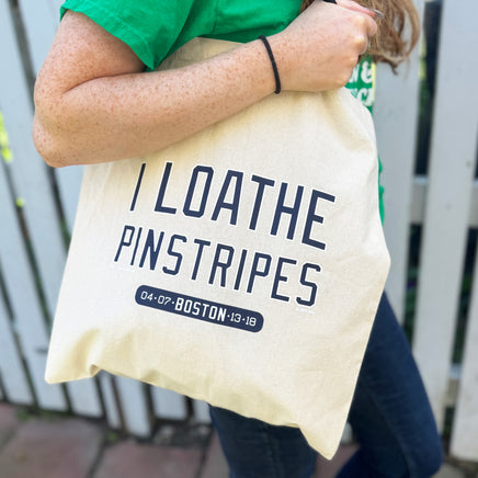 woman holding tan canvas tote bag with the red sox phrase i loathe pinstripes by the red seat