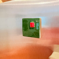 Green square magnet with a red center on a stainless steel refrigerator