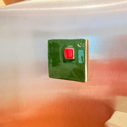 Green square magnet with a red center on a stainless steel refrigerator