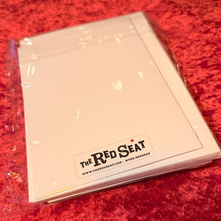 Stack of white cards with 'The Red Seat' logo on a red textured surface