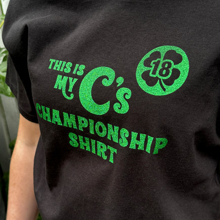 person wearing Black unisex t-shirt with the words this is my C's championship shirt in glittery green lettering