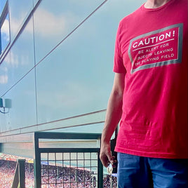 photo of a man at boston fenway park wearing Red unisex t-shirt with fenway park caution warning in white text