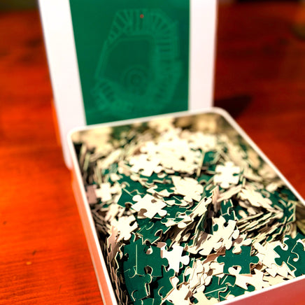 Jigsaw puzzle pieces in a box with a green and white design on a wooden surface