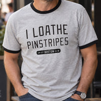 Man wearing heather gray I Loathe Pinstripes Red Sox ringer tee with black trim and jeans outside a Boston cafe
