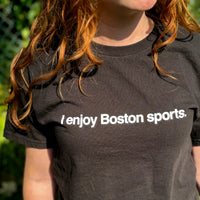 photo of a woman wearing black unisex t-shirt with the words i enjoy boston sports in white text