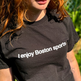 photo of a woman wearing black unisex t-shirt with the words i enjoy boston sports in white text