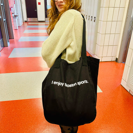 photo of woman holding black tote bag with the words "i enjoy boston sports" written in white helvetica font
