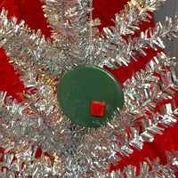 Close-up of silver tinsel tree with a green and red porcelain ornament on a red background