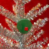 Close-up of silver tinsel tree with a green and red porcelain ornament on a red background