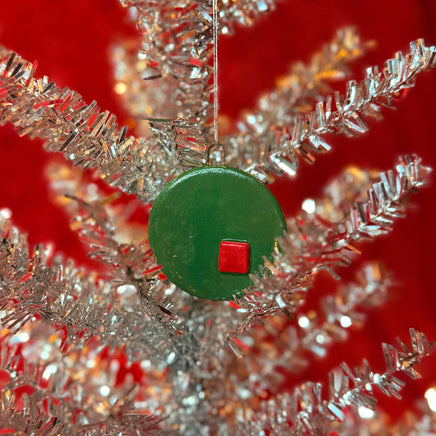 Close-up of silver tinsel tree with a green and red porcelain ornament on a red background