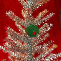 Close-up of silver tinsel christmas tree with a green and red porcelain ornament on a red background