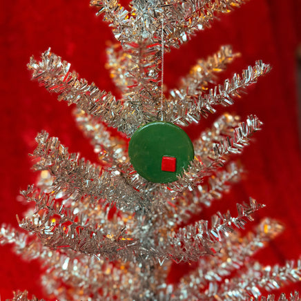 Close-up of silver tinsel christmas tree with a green and red porcelain ornament on a red background