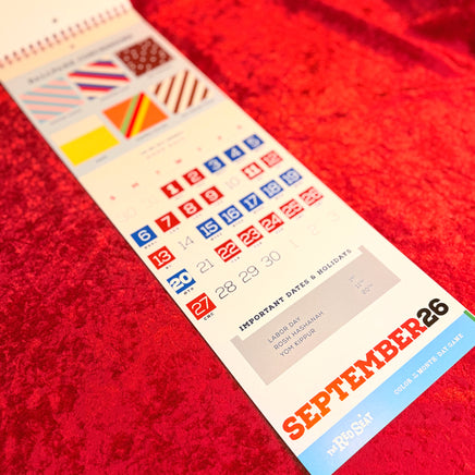 The Red Seat Calendar with colorful design on a red textured surface