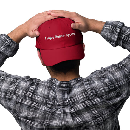 man wearing red baseball cap with "i enjoy boston sports" embroidered in white helvetica font