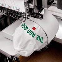 White cap with 'The Red Seat' text being embroidered on a machine.