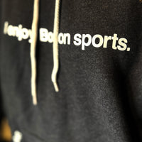 close up of black unisex hoodie with the words i enjoy boston sports in white with the red seat logo