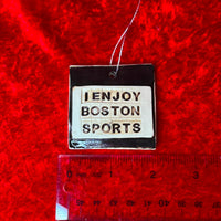 photo of round white and black porcelain ornament that says, i enjoy boston sports on red background with a ruler