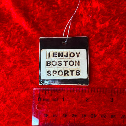 photo of round white and black porcelain ornament that says, i enjoy boston sports on red background with a ruler