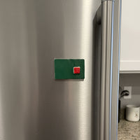 Green square magnet with a red center on a stainless steel refrigerator