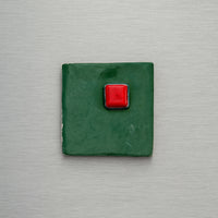 Green square magnet with a red button on a metallic surface