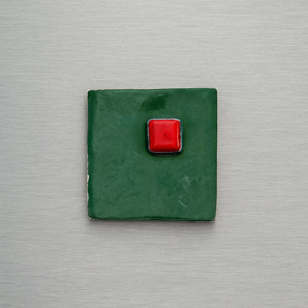 Green square magnet with a red button on a metallic surface