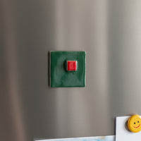 Green square magnet with a red button on a metallic surface