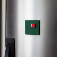 Green square magnet with a red button on a metallic surface